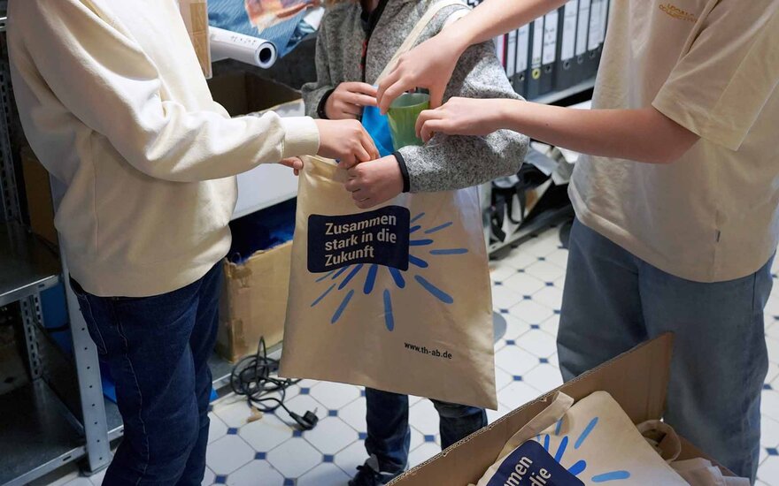 Drei Jungen packen beim Boys Day im Marketing Give-aways in eine TH-Tasche