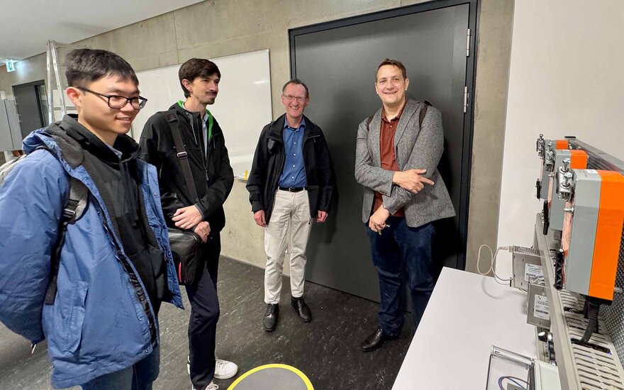 Vier Männer im Halbkreis blicken auf ein technisches Gerät
