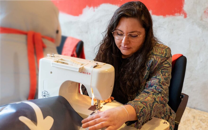 Alexandra Koch sitzt an einer Werkbank in der Nähwerkstatt des Gesta e.V. und näht an einem alten Werbebanner.