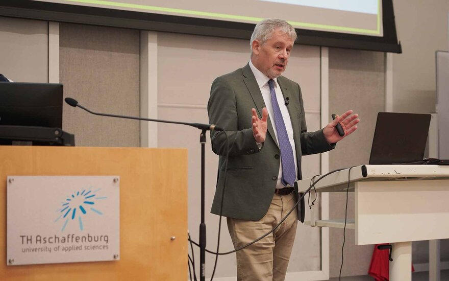 Ein Mann im Anzug steht hinter einem Rednerpult und gestikuliert mit den Händen.