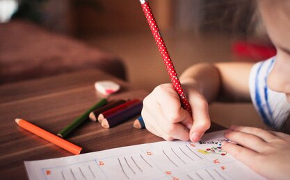 Kleinkind malt ein Blatt an einem Tisch aus
