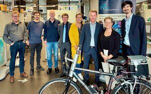 Teilnehmende des Treffens bei der Besichtigung des Labors für Dynamik und Schwingungstechnik, acht Personen stehen nebeneinander, im Vordergrund ist ein Fahrrad zu sehen