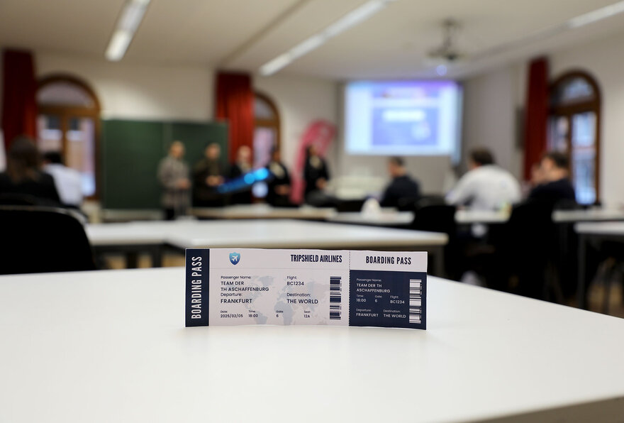 Ein Flugticket ist im Vordergrund während im Hintergrund das MKD Pitch-Event stattfindet