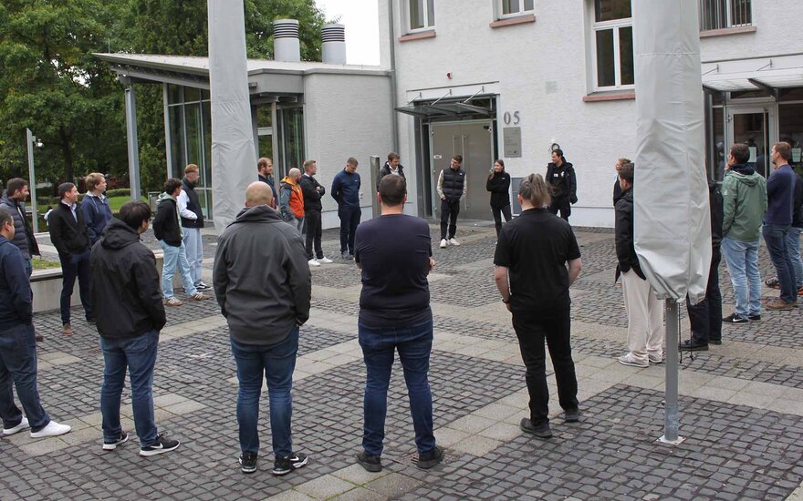 Berufsbegleitende Studierende stehen im Kreis vor dem weißen Mensagebäude