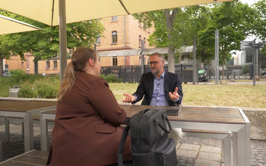 Professor Lars Schöne unterhält sich mit einer Studentin an einem Tisch auf dem Hochschulcampus