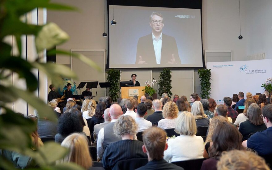 Leinwand mit Staatsminister vor sitzenden Personen in der Aula