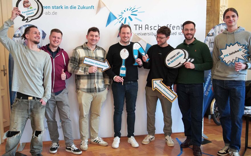 Gruppenfoto mit Timm und 6 Kommilitonen, alle halten lustige Schilder mit Sprüchen oder Symbole aus Pappe in der Hand