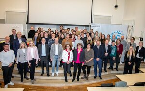 Fördernde, Stipendiatinnen und Stipendiaten stehen in der Aula der Hochschule in mehreren Reihen nebeneinander auf der Bühne, im Hintergrund ist ein Teil des blauen TH-Logos zu sehen