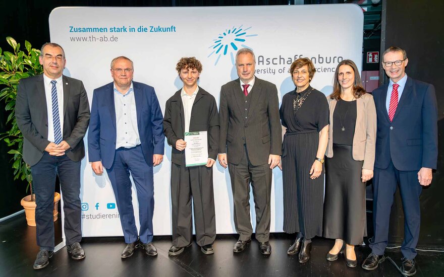 Gruppenbild mit 7 Personen in festlicher Kleidung vor weißer TH-Logowand