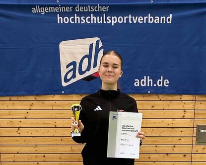 Siegerin Anna Braun mit Urkunde und Pokal in der Hand vor Hochschulverbandsbanner