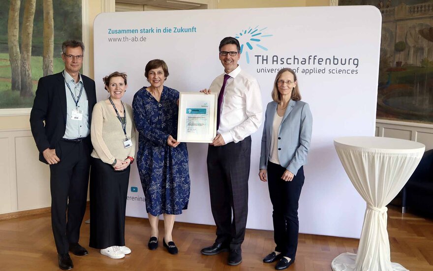 Gruppenfoto vor TH-Logo-Wand im Hocksaal mit zwei Männern und drei Frauen