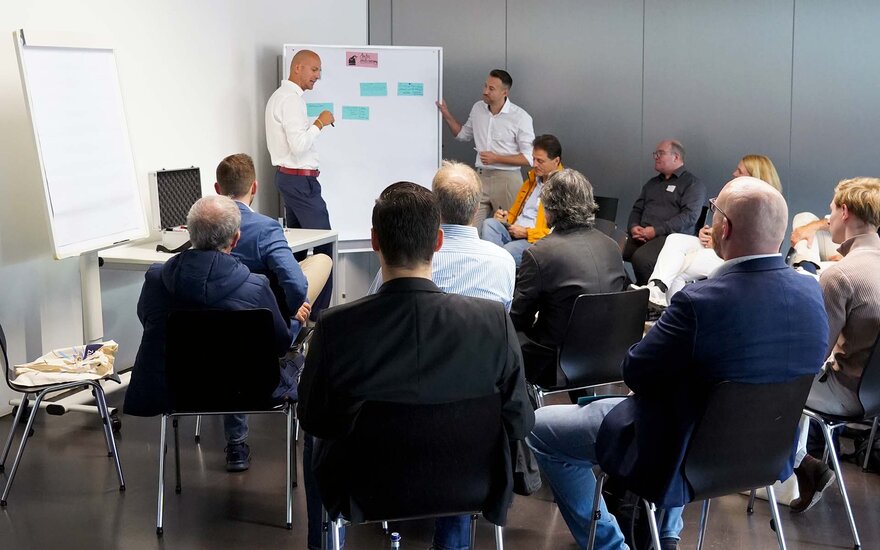 Gruppe von sitzenden Teilnehmenden bei Workshop, zwei Personen stehen am Flipchart.