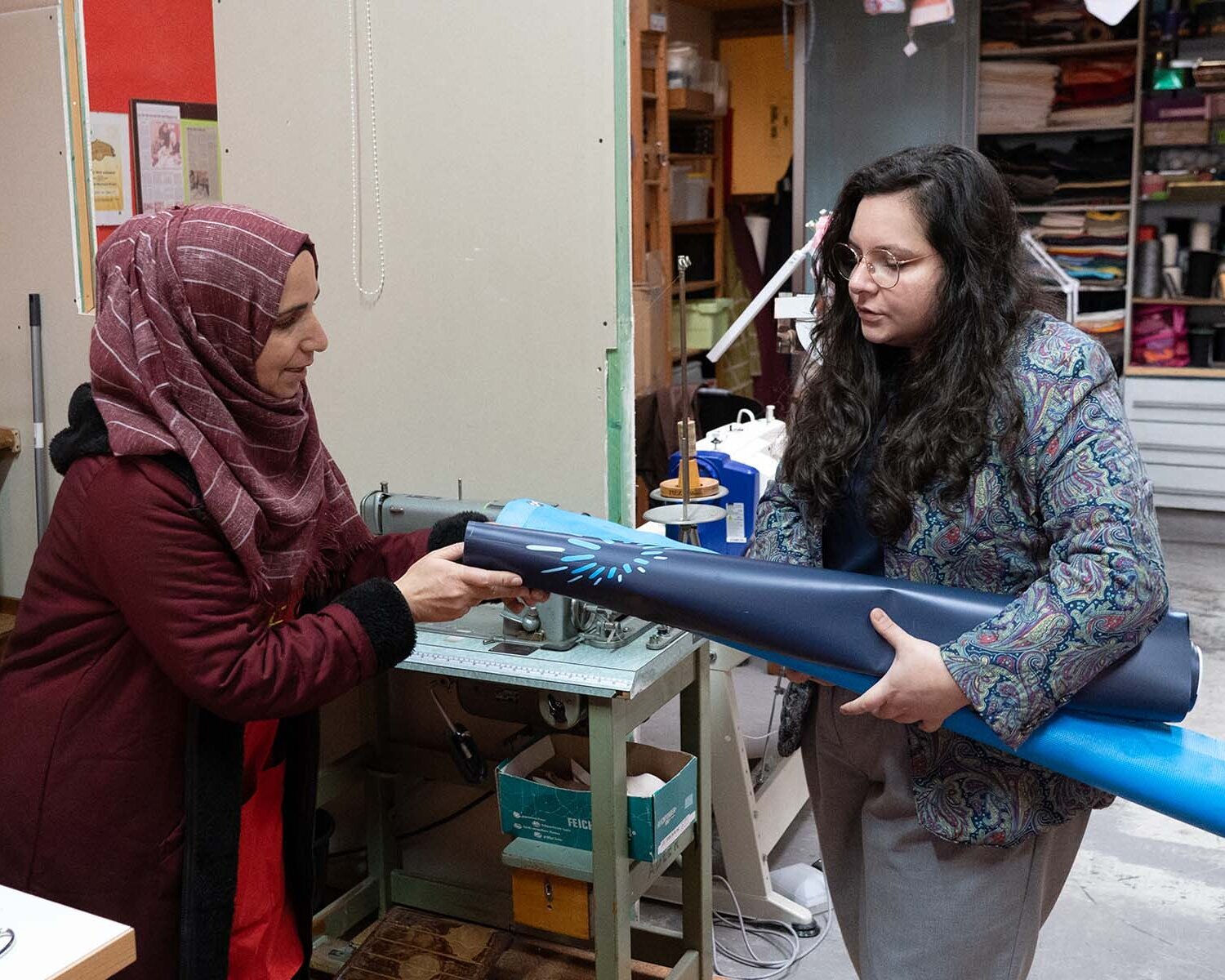 In der Nähwerkstatt übergibt Alexandra Koch Amina von Gesta e.V. alte, blaue Werbebanner der TH Aschaffenburg