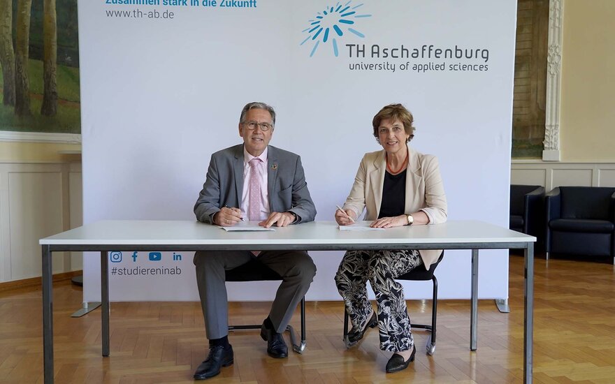 Oberbürgermeister im grauen Anzug und TH-Präsidentin im beigen Blazer unterzeichnen im Sitzen am Tisch Vertrag