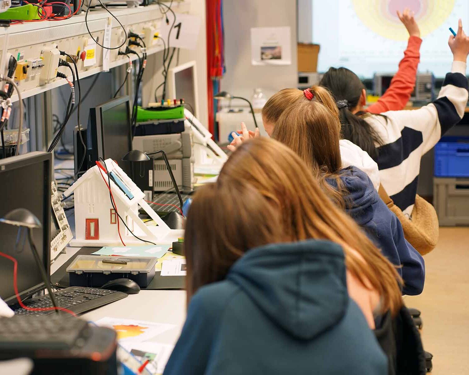 Mehrere Mädchen sitzen nebeneinander an Tischen mit Modellhäusern und technischer Ausstattung.