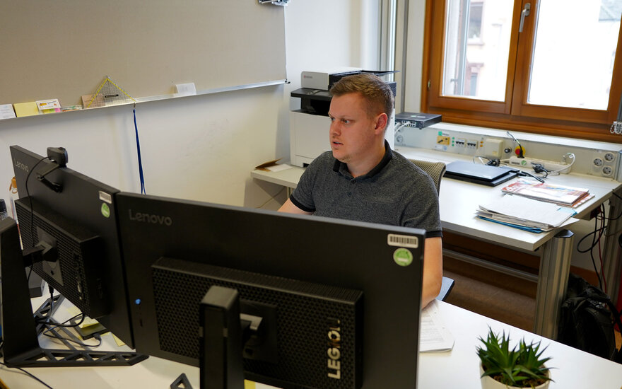 Luca Spielmann sitzt an seinem Arbeitsplatz und schaut auf einem seiner zwei Computerbildschirme.