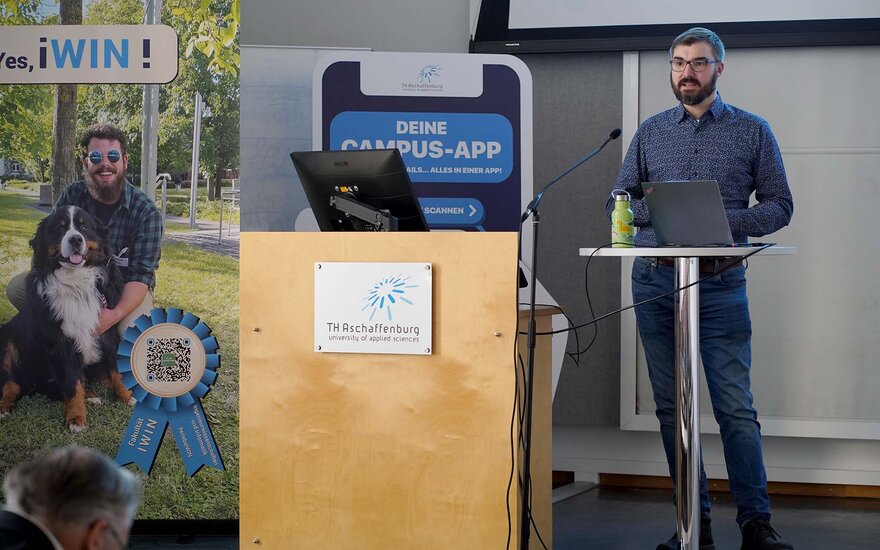 Professor Keil am Rednerpult neben dem Banner der Fakultät IWIN