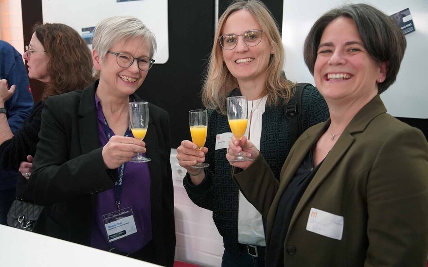 Drei Fakultätsmitarbeiterinnen stoßen mit O-Saft an und lächeln