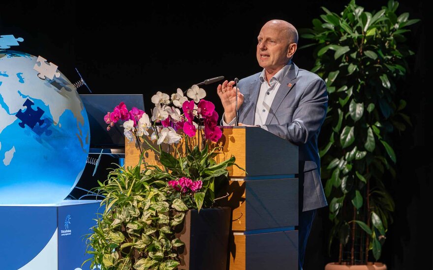 Mann mittleren Alters mit Glatze im grauen Anzug am Rednerpult