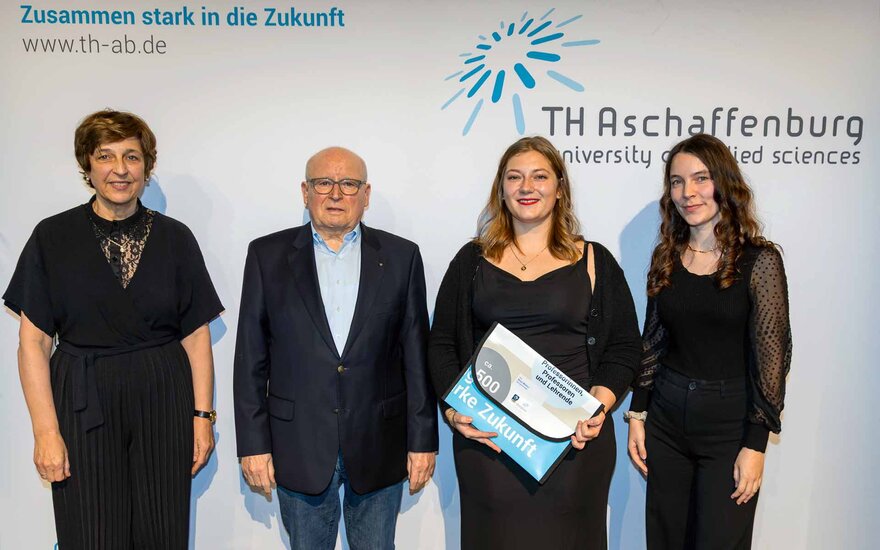 Junge Frau mit blonden schulterlangen Haaren eingerahmt von einem Mann und zwei Frauen in schwarzer Kleidung