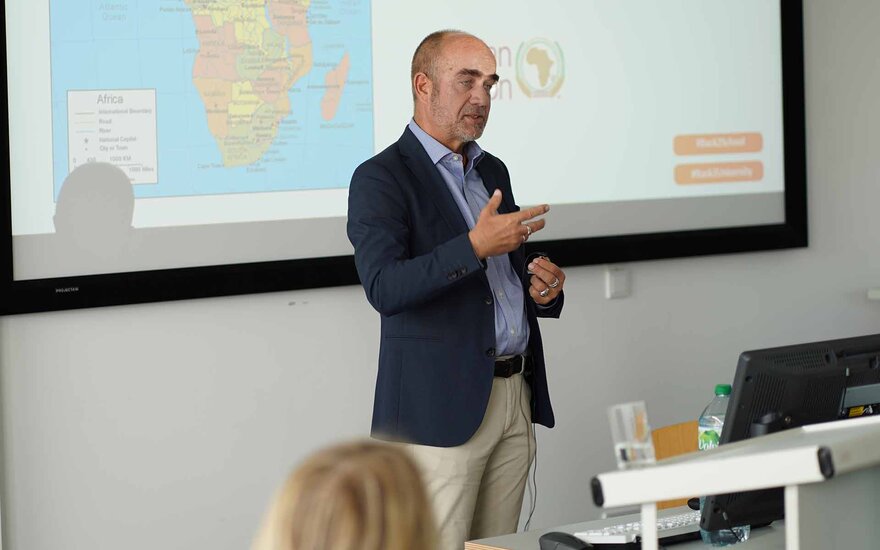 Gastreferent Matthias Reusing am Rednerpult vor Leinwand mit Weltkarte