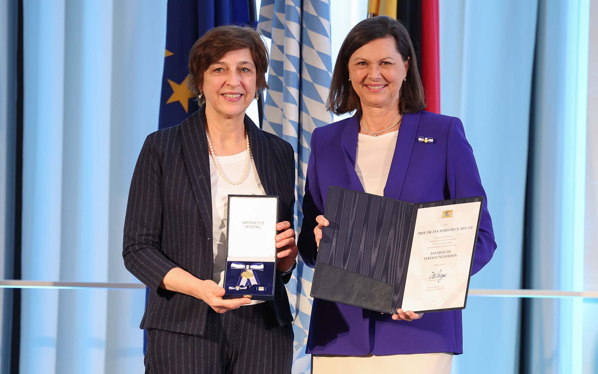 Landtagspräsidentin Aigner überreicht TH-Präsidentin Beck-Meuth den Orden. Beide schauen lächelnd in die Kamera.