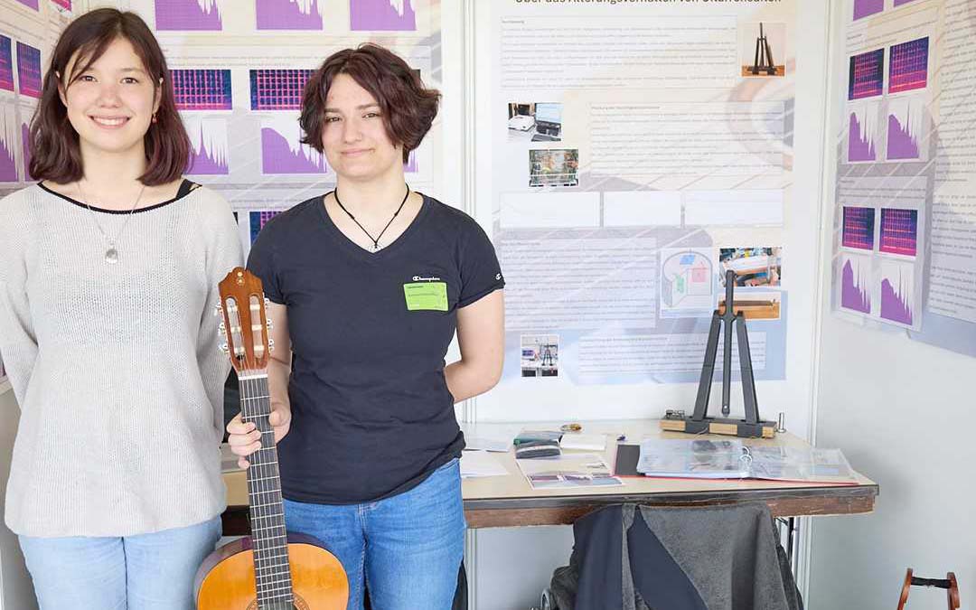 Anna und Susanne stehen nebeneinander und halten eine Gitarre in den Händen