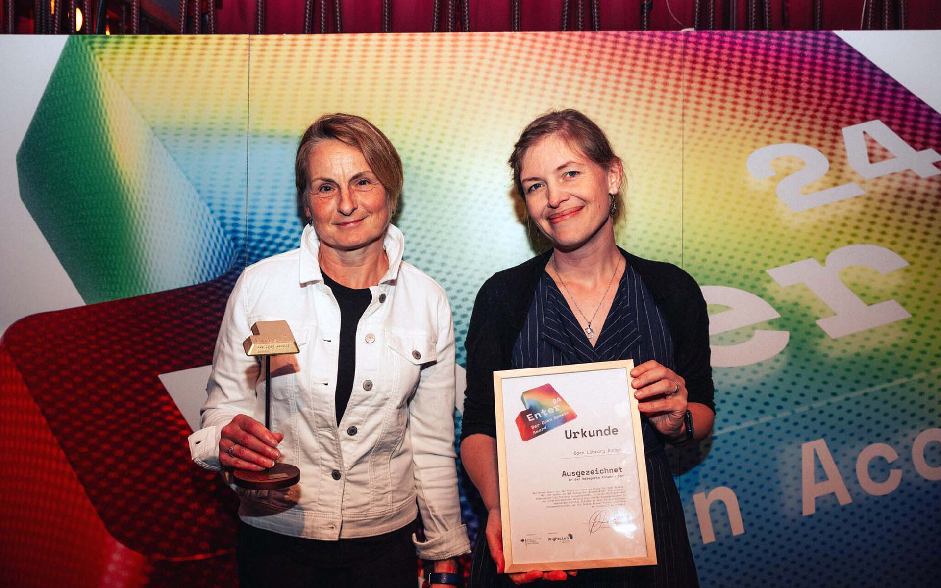 Zwei Frauen halten lächelnd Preis und Urkunde in den Händen.
