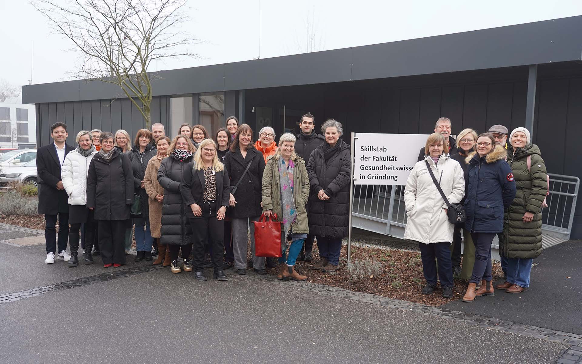 Gruppenfoto der Teilnehmenden vor dem Schild und Container der Fakultät Gesundheitswissenschaften.