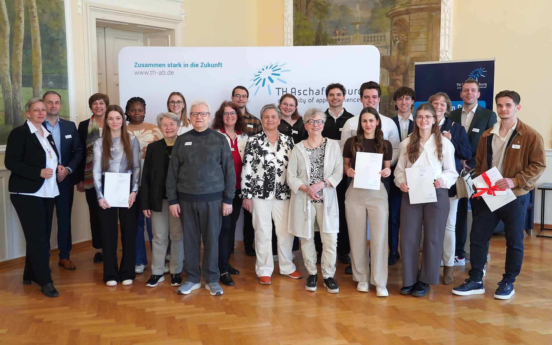Gruppenfoto von Stipendiaten und Fördernden im Hocksaal vor TH-Logo-Wand
