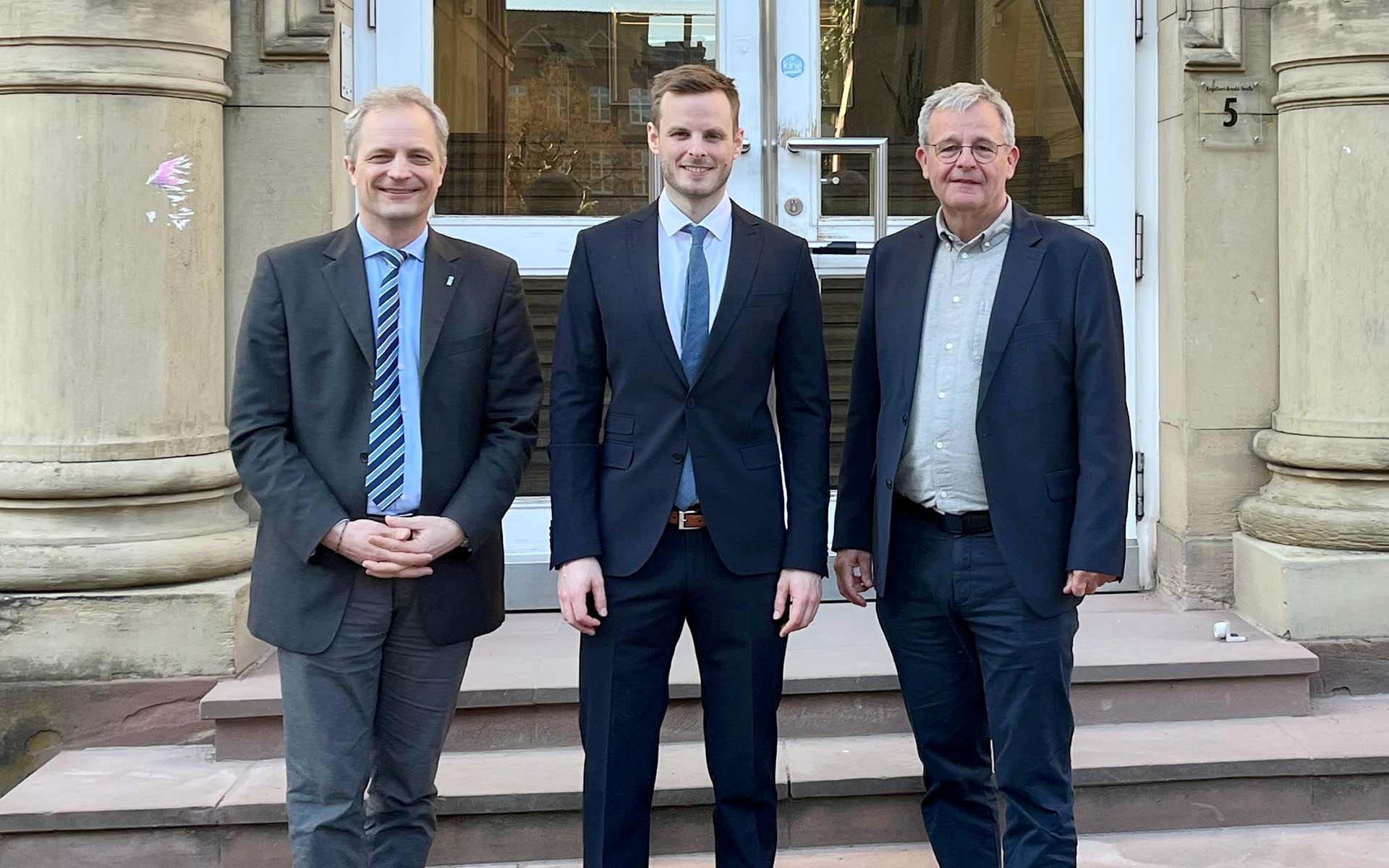 Johannes Büdel im schwarzen Anzug zwischen beiden Professoren vor Eingang des Instituts