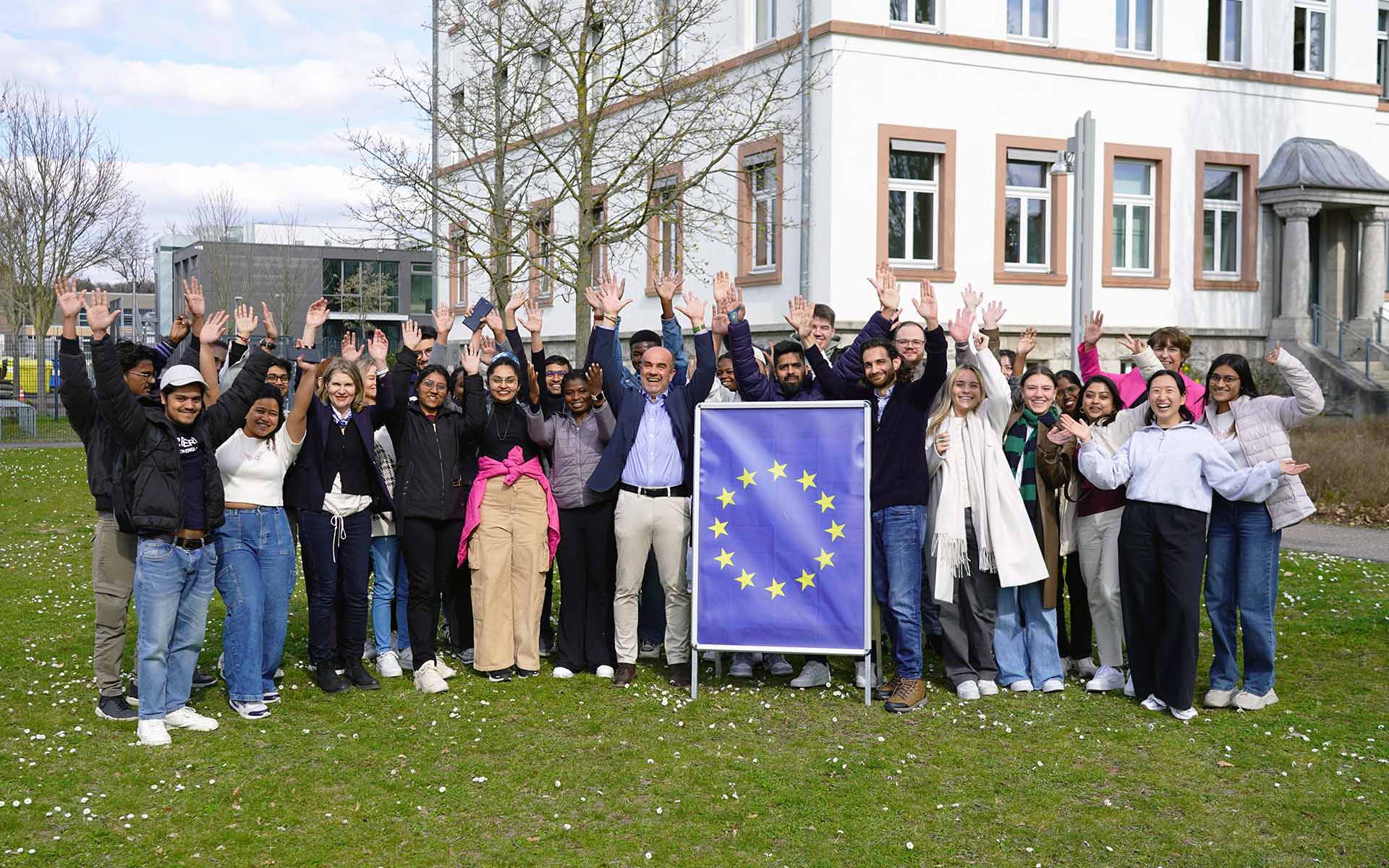 Gruppe der Studierenden mit Gastreferent, EU-Schild und alle heben die Hände