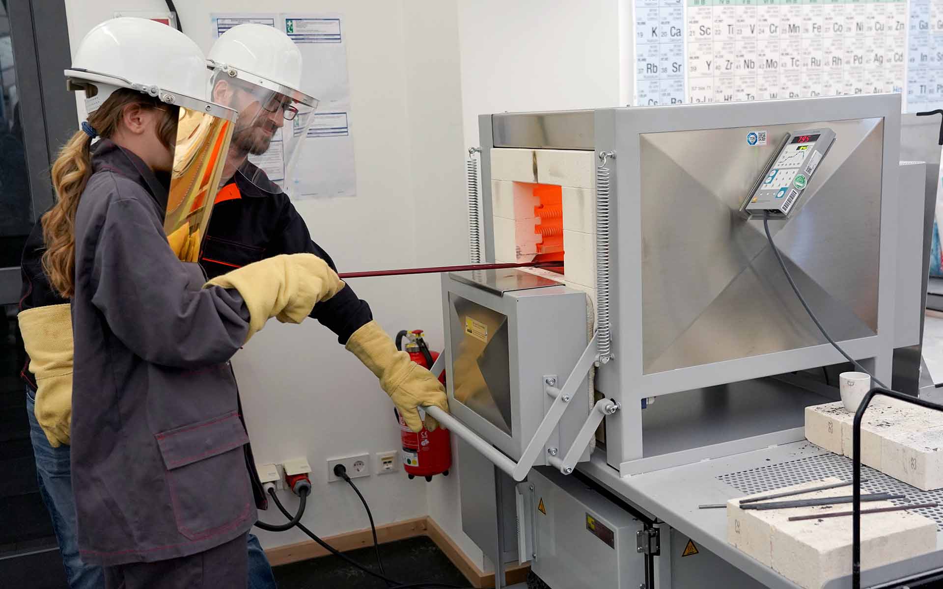 Teilnehmerin des Girls Days mit Helm und Schutzkleidung am Brennofen mit Labormitarbeiter