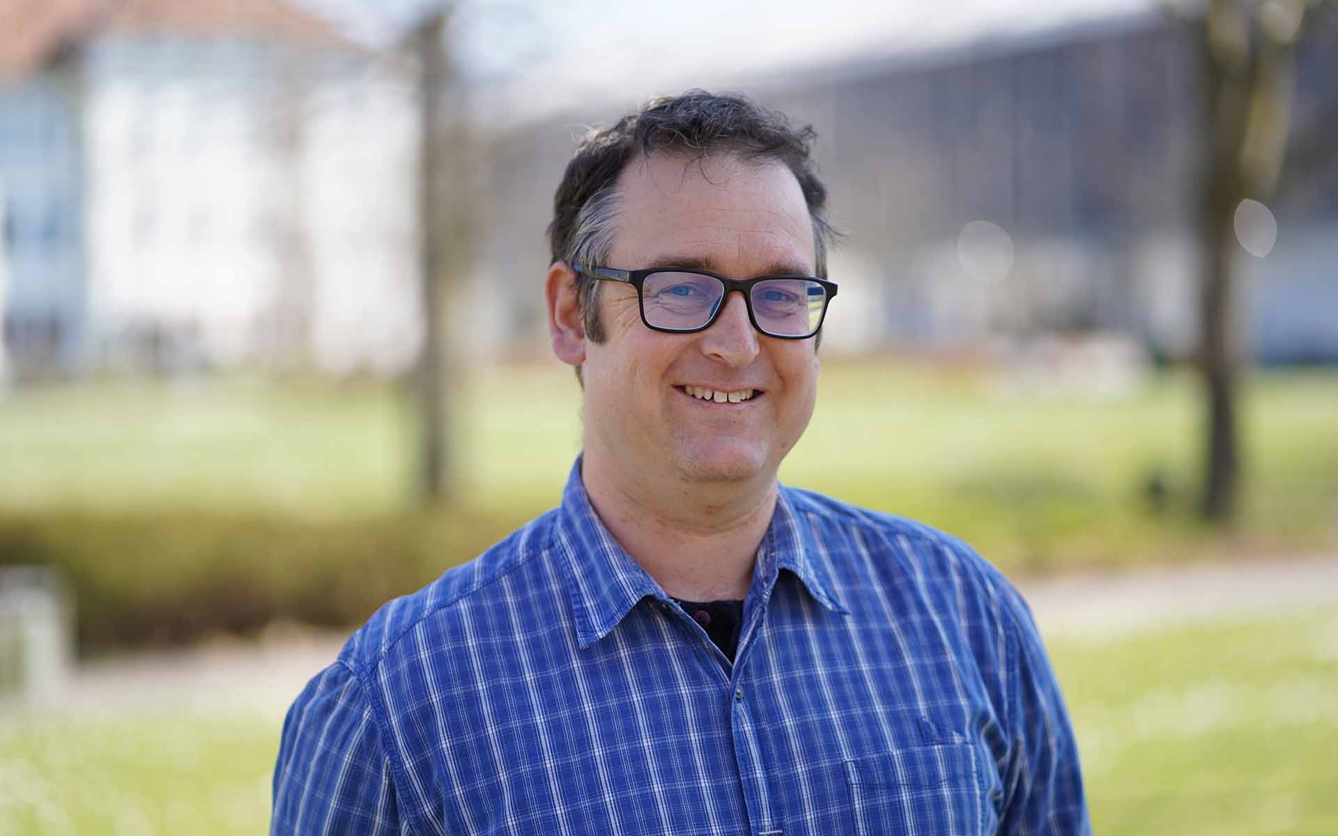 Hendrik Arend mit Brille im blauen Hemd vor der Campuswiese und TH-Gebäuden