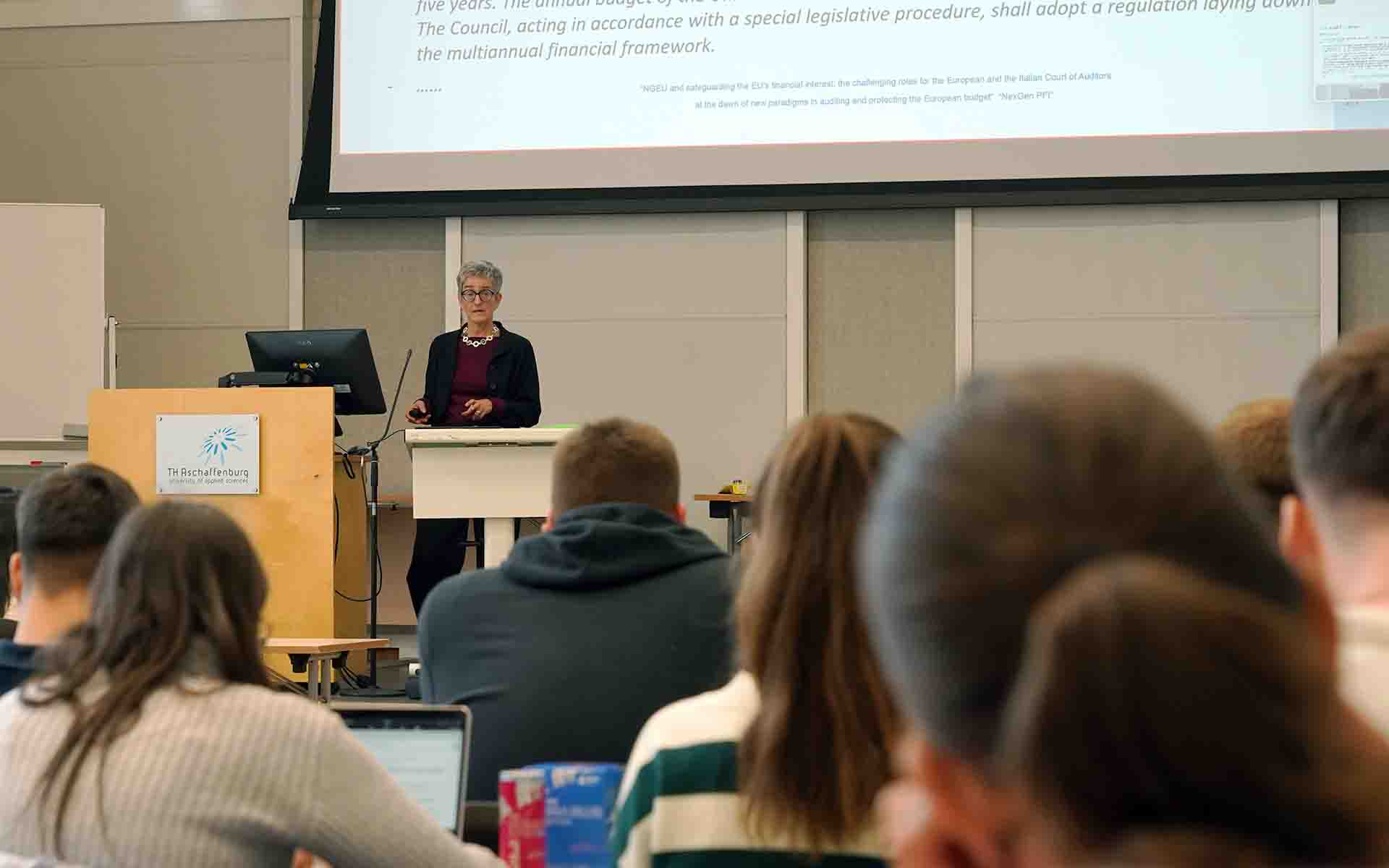 Professorin Balleis am Rednerpult vor Leinwand mit Studierenden im Vordergrund