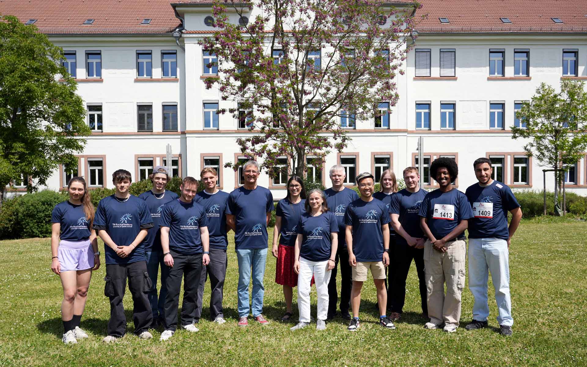 Laufteam der TH AB mit blauen T-Shirts auf Campuswiese vor weißem Gebäude 20