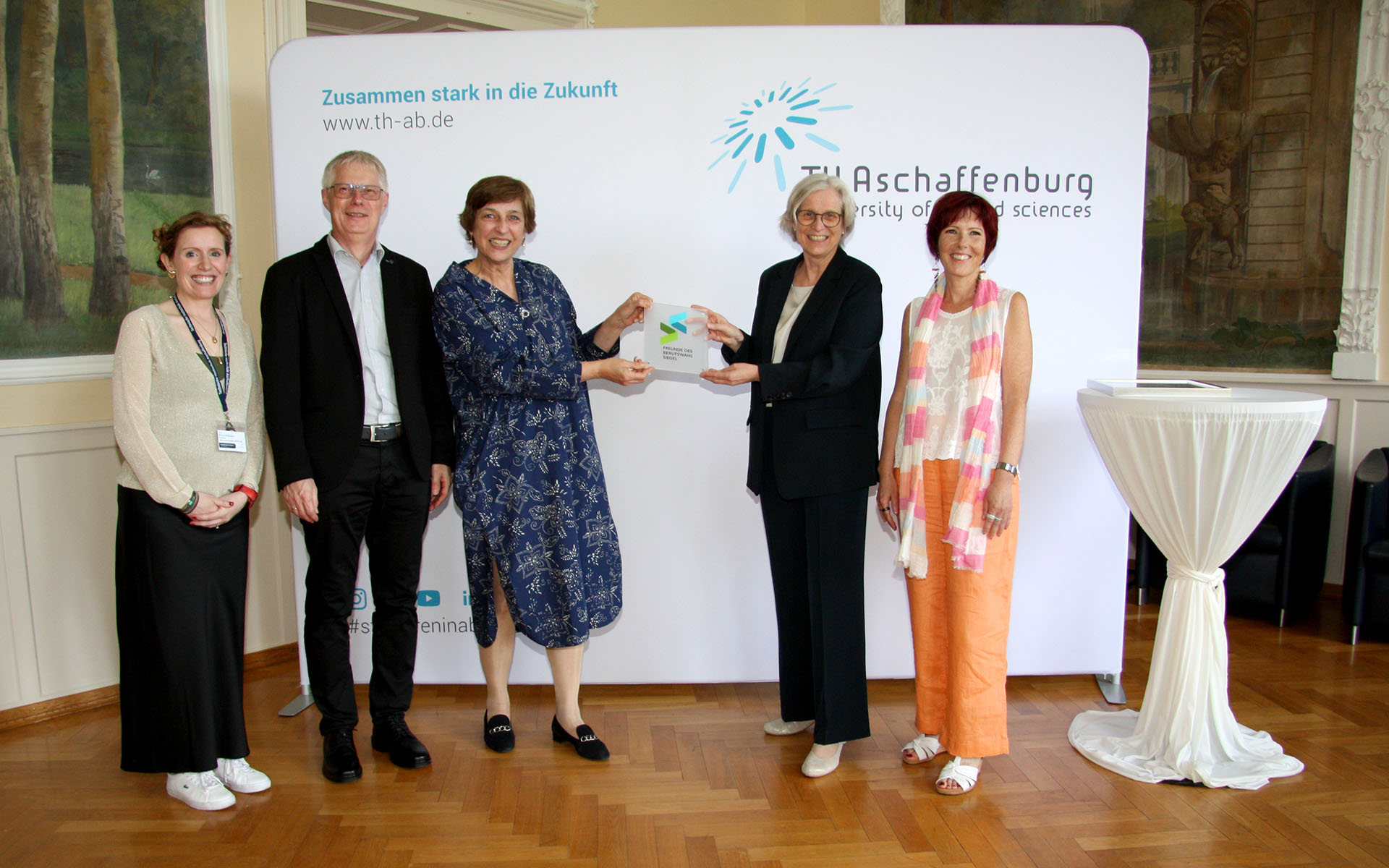 Gruppenfoto vor TH-Logo-Wand im Hocksaal mit einem Mann und vier Frauen