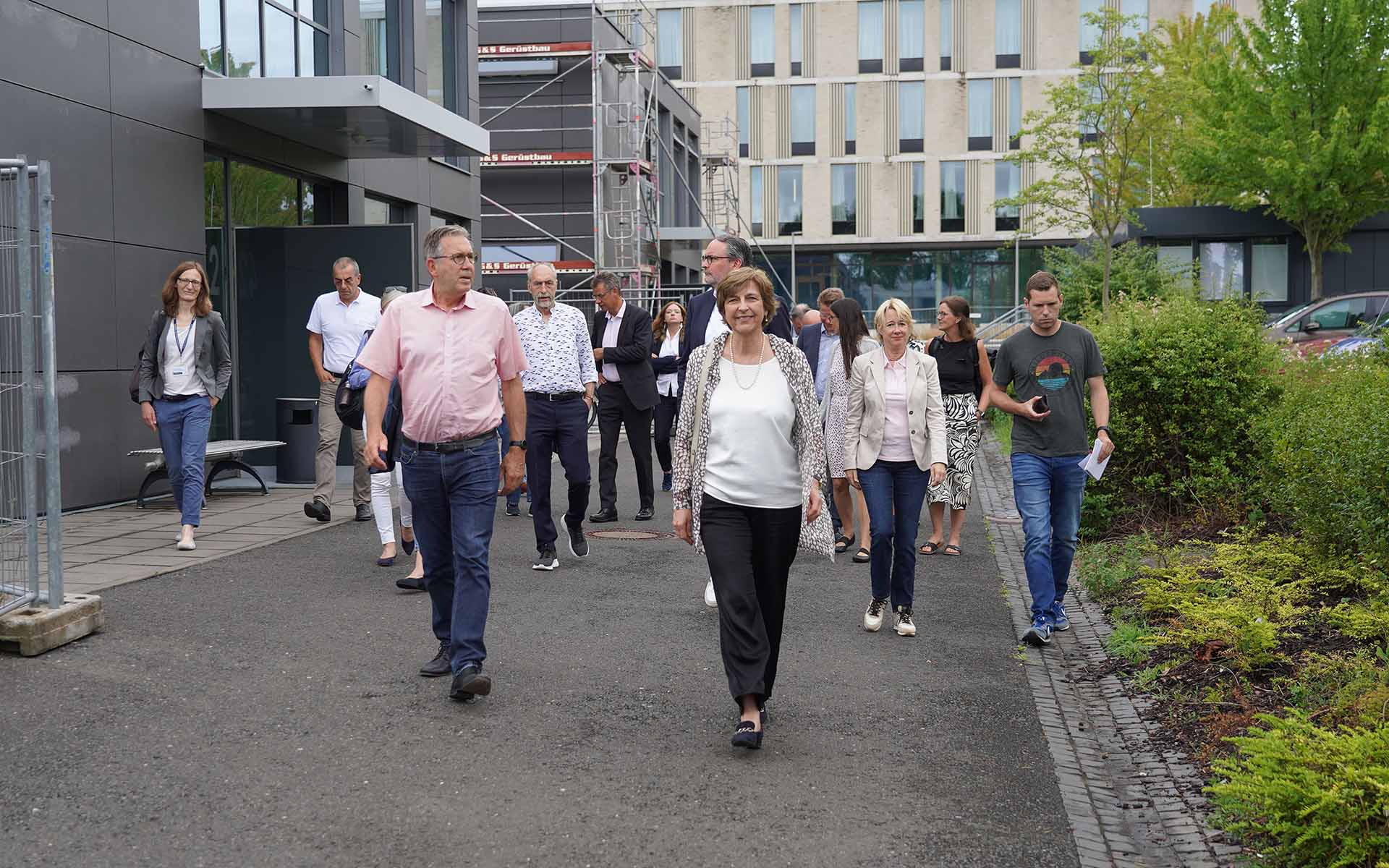 Präsidentin und Oberbürgermeister laufen mit Stadratsmitgliedern auf Weg vor Neubauten
