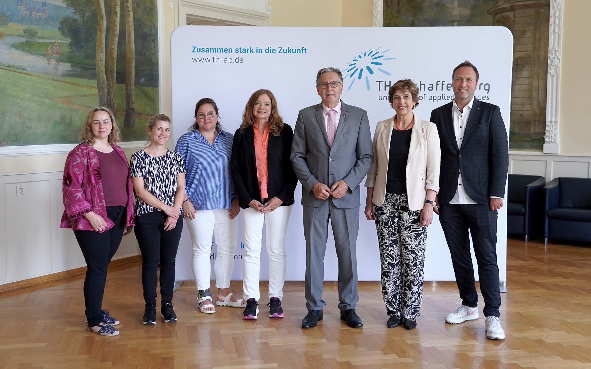 Fünf Frauen und zwei Männer stehen nebeneinander vor weißer Messewand mit blauem TH-Logo im Hocksaal