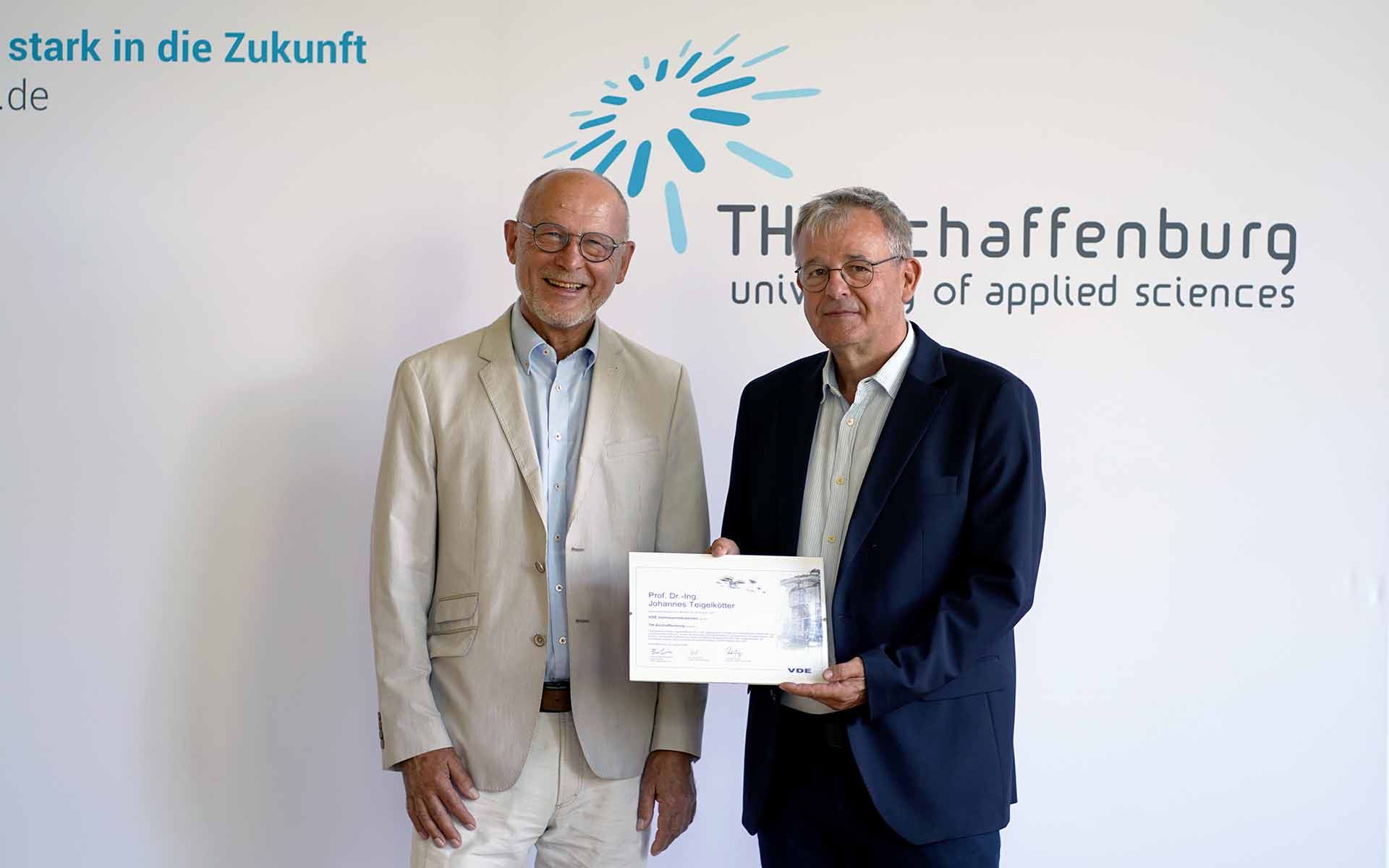 VDE-Geschäftsführer und VDE-Vertrauensdozent mit Urkunde vor TH-Logowand