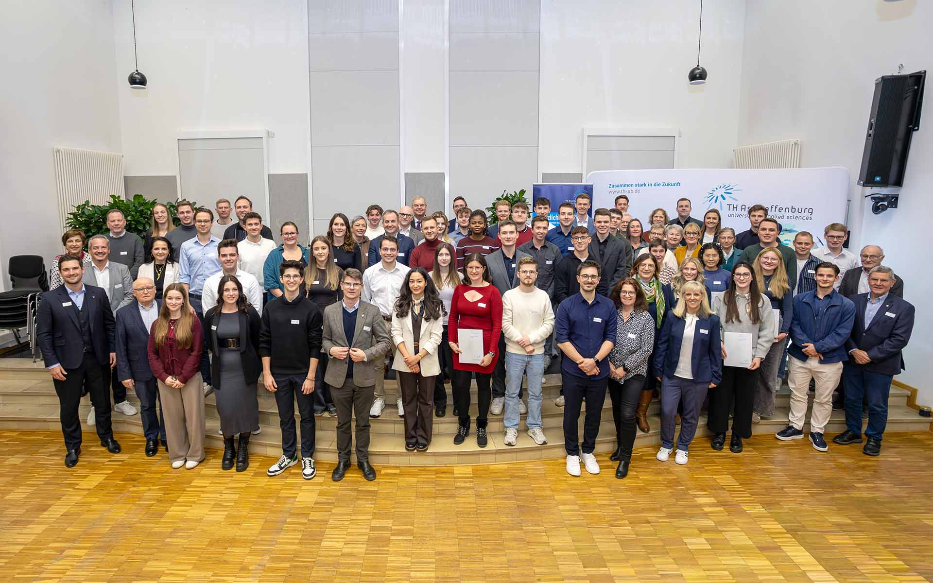 Gruppenbild mit den Fördernden und Stipendiaten in der Aula vor TH-Logowand