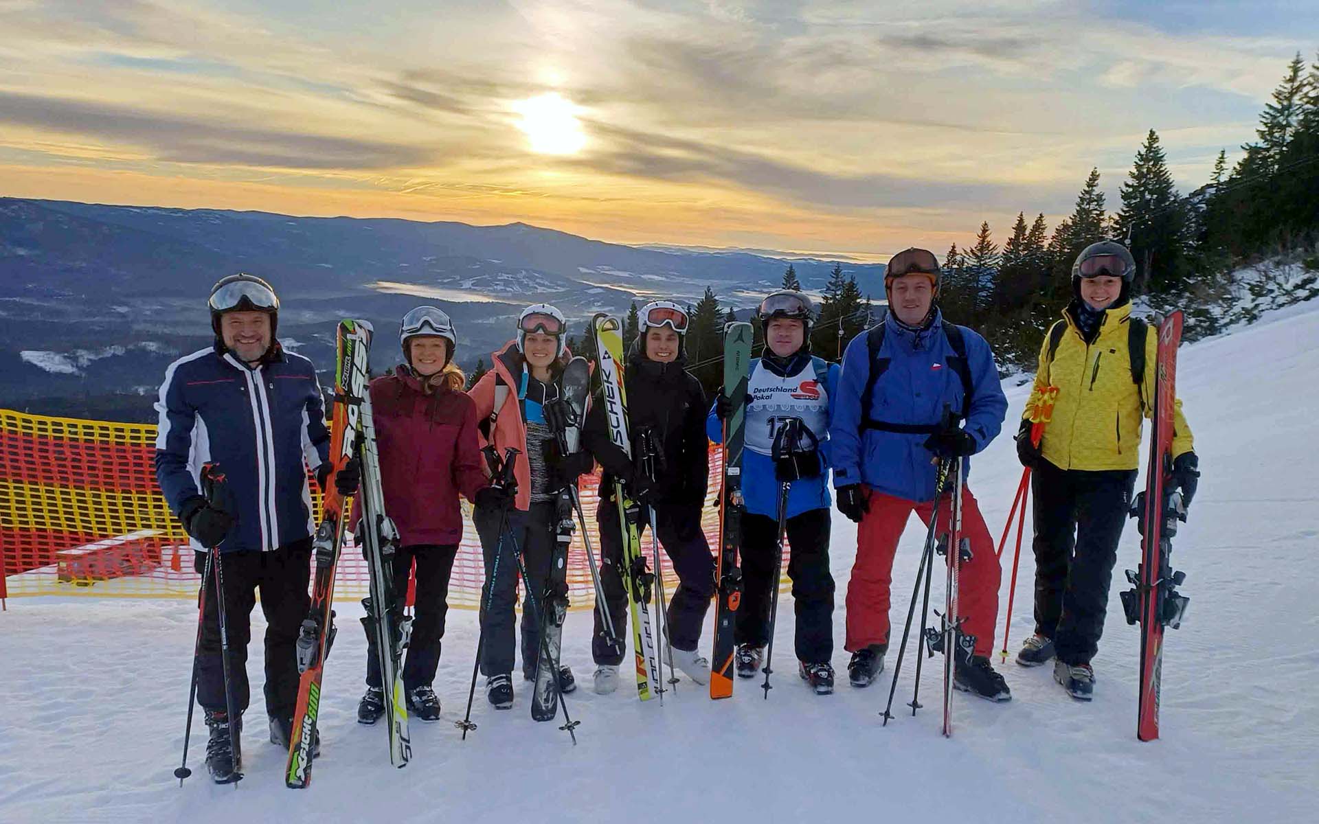 Sieben Personen stehen in Skiausrüstung mit Ski in der Hand auf der Piste. 