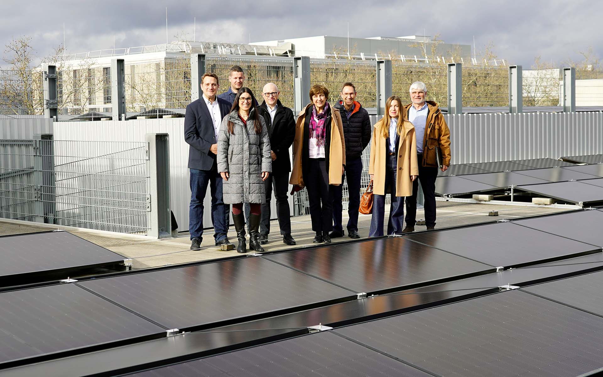 Gruppe von acht Personen steht auf dem Parkhausdach hinter der Solarpanelfläche