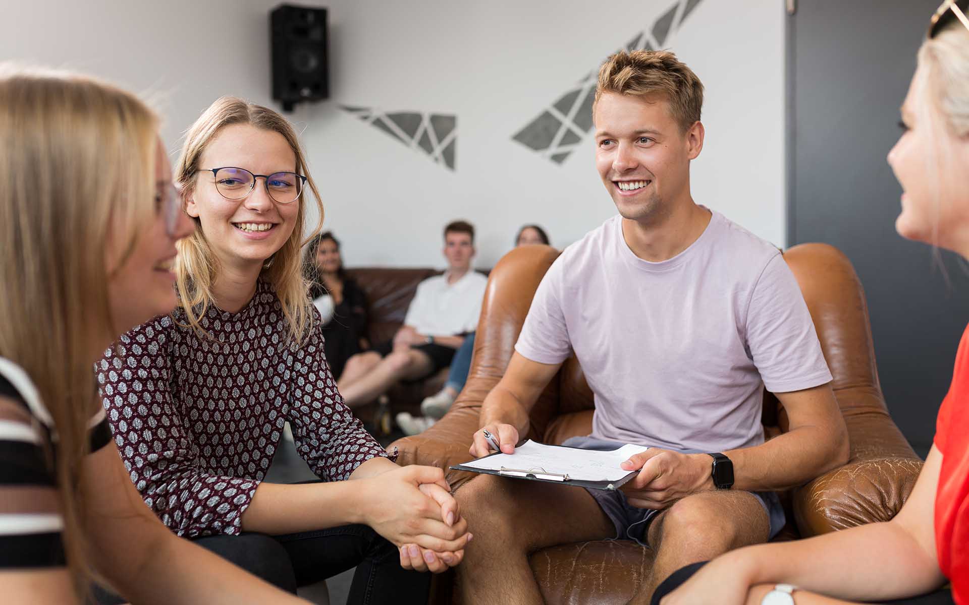 Drei Studentinnen und ein Student sitzen zusammen und unterhalten sich lächelnd