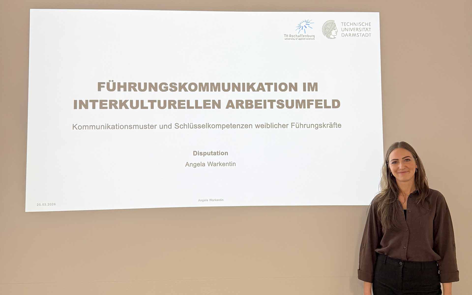 Frau mit langen dunkelblonden Haaren steht vor Leinwand mit Titel ihrer Promotion