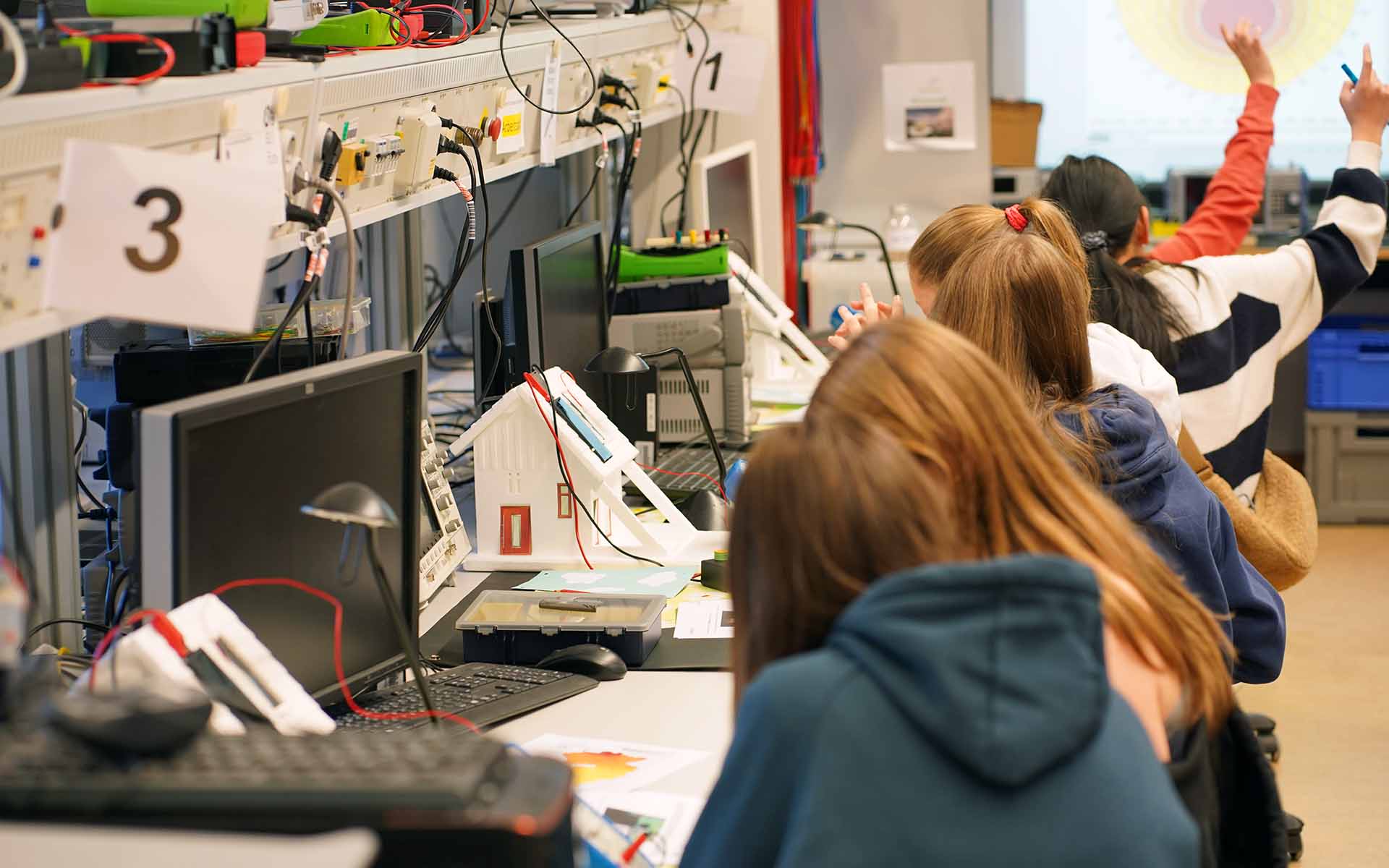 Mehrere Mädchen sitzen nebeneinander an Tischen mit Modellhäusern und technischer Ausstattung.