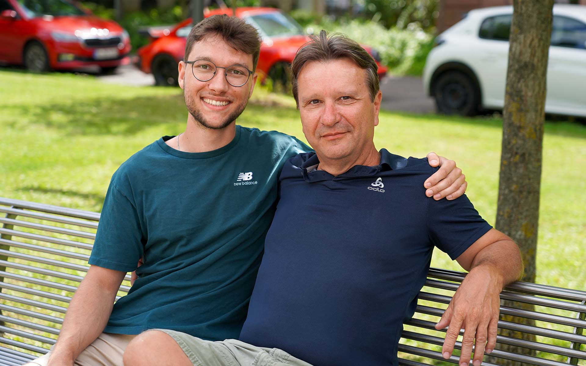 Vater und Sohn sitzen nebeneinander auf einer Bank am Campus